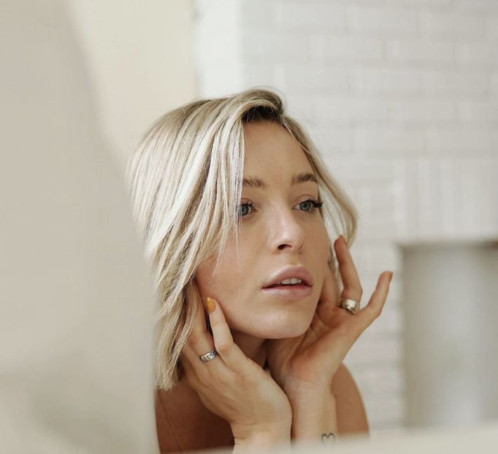 Woman with luminous, healthy skin admiring her reflection — skin rejuvenation results at Remedy+ Grand Rapids MI